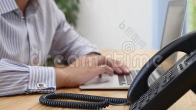 在工作区的桌面键盘上`商人的手。 焦点是<strong>座机电话</strong>，背景模糊.. 关门